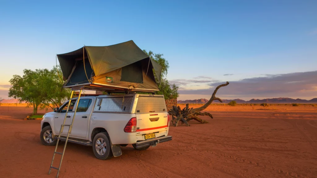 Toyota Hilux equipped with a rooftop tent nestled amidst the serene Namibian desert, showcasing a perfect blend of adventure and comfort for a memorable camping experience.